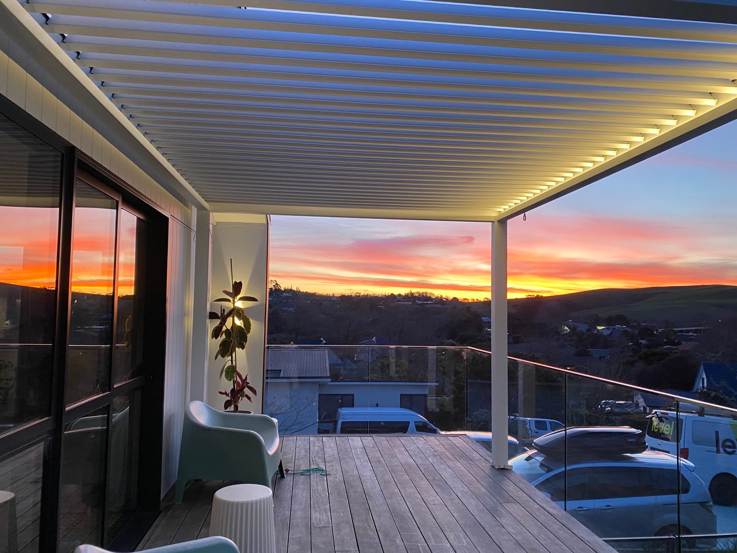 Balcony with louvred pergola, wooden floor and glass walls during sunset